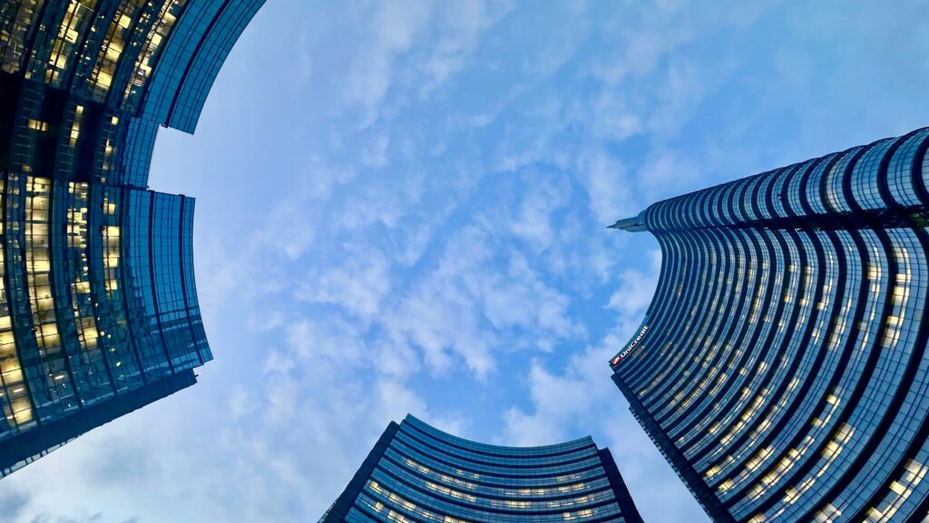 Upward view of UniCredit Tower in Milan with dramatic sky and modern architecture.